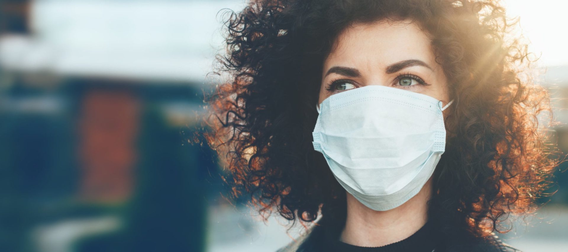 Lovely curly haired caucasian lady protecting herself from viruses while wearing special mask